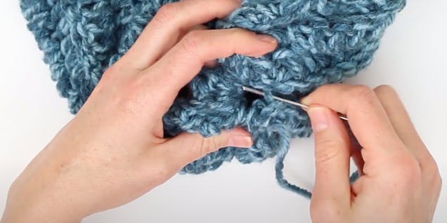 darning needle sewing together the top of the crochet hat