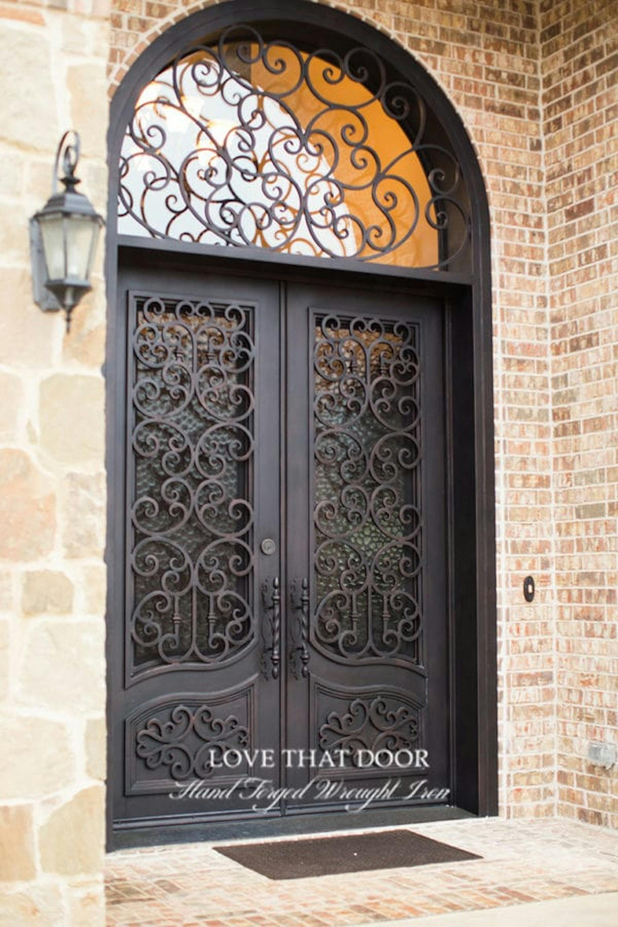 Impressive iron door with transom featuring intricate scrollwork and glass accents.
