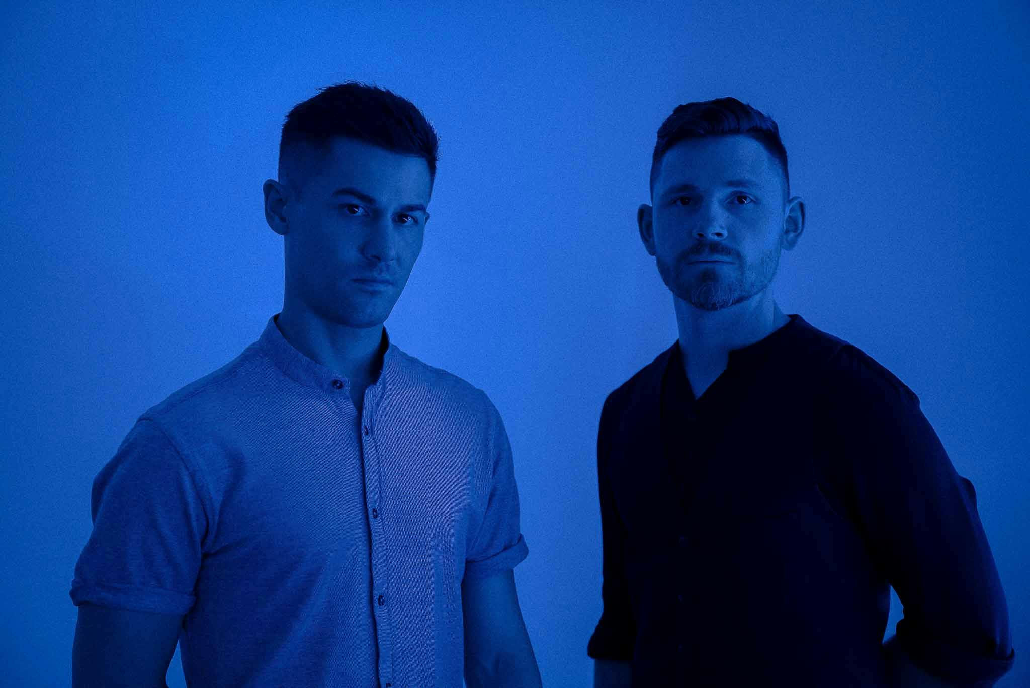 Zack Gray standing with his brother on a blue background promoting his new song 'Whatever it Takes'.