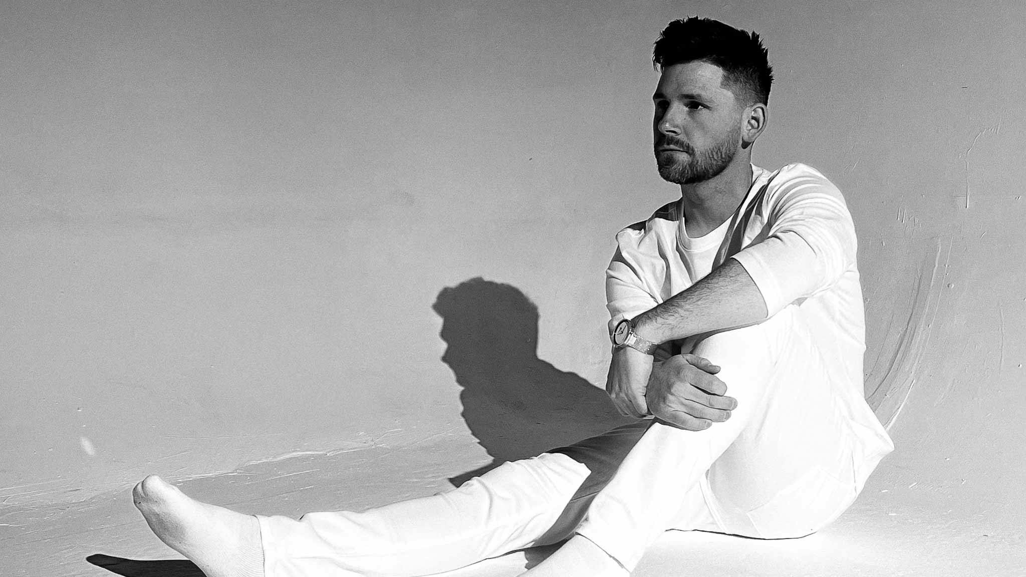 DJ and musician, Zack Gray sitting down while wearing a white outfit in a photography studio