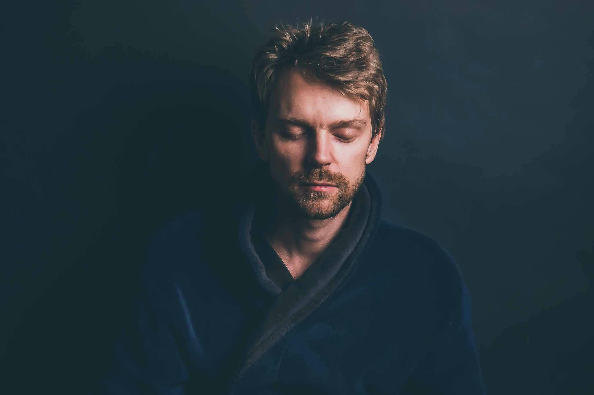 Man sitting alone in a blue robe meditating quietly with his eyes shut