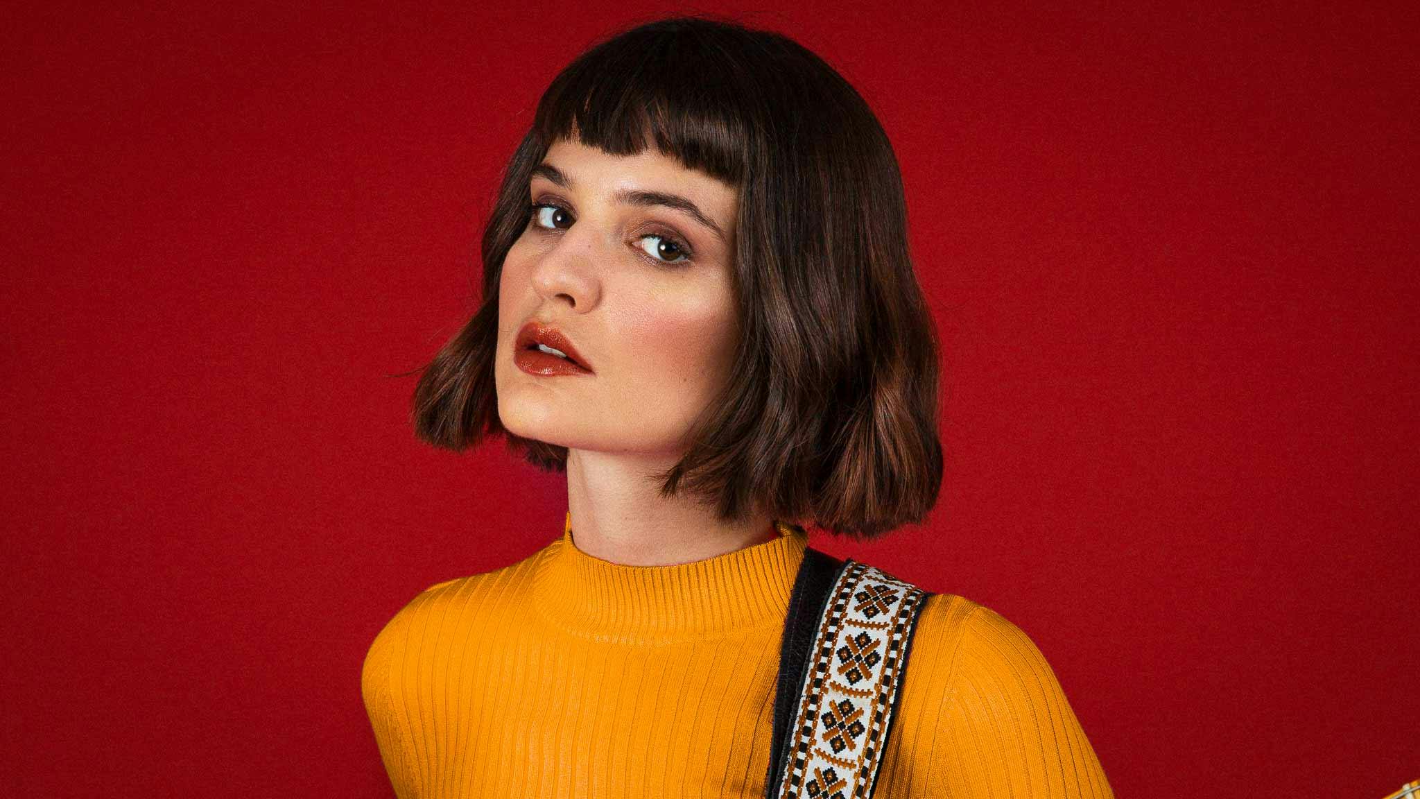 Violetta Zironi standing in front of a red wall wearing a yellow sweater