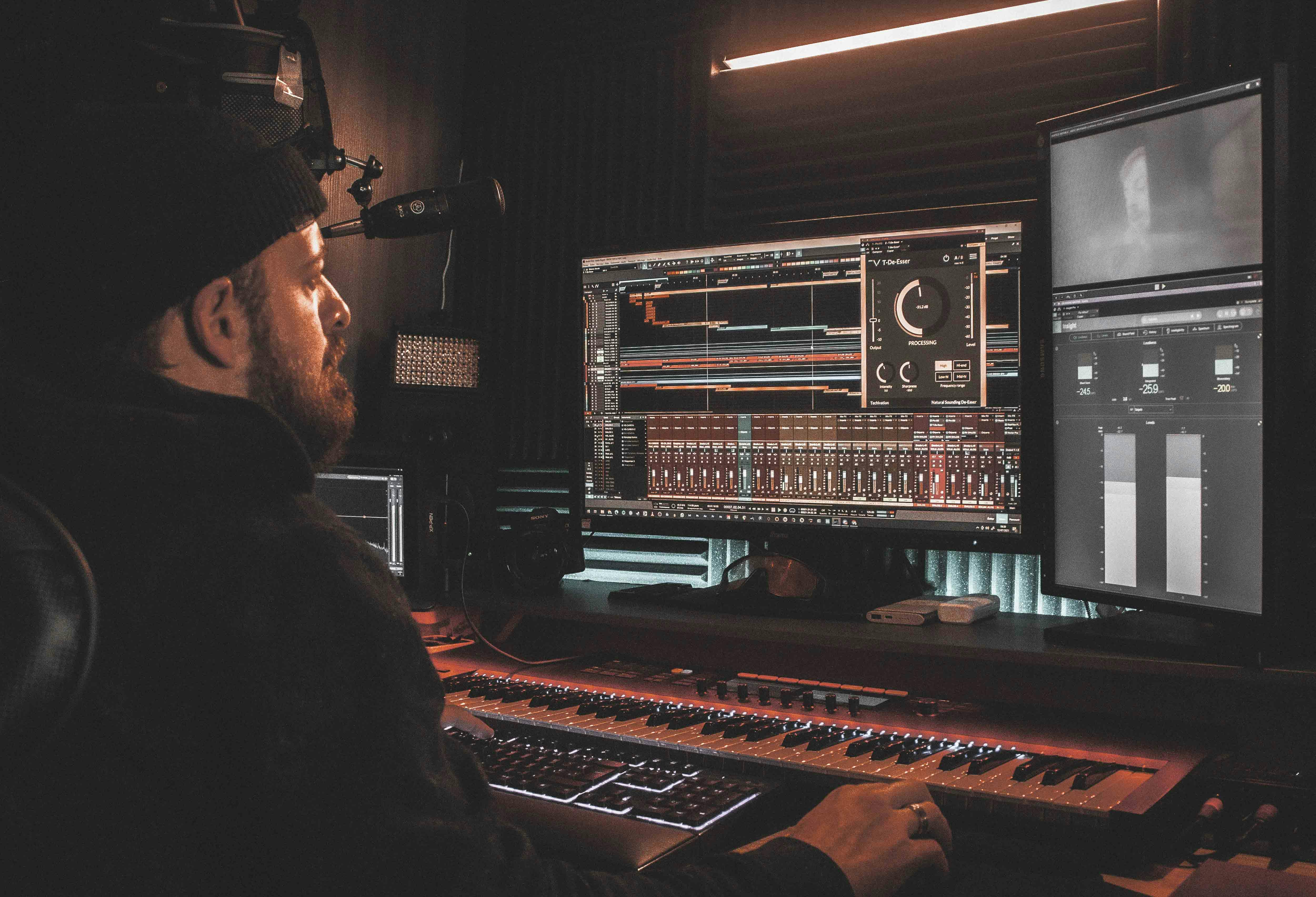 A man in a beanie sitting at his music workstation recording music through a DAW.