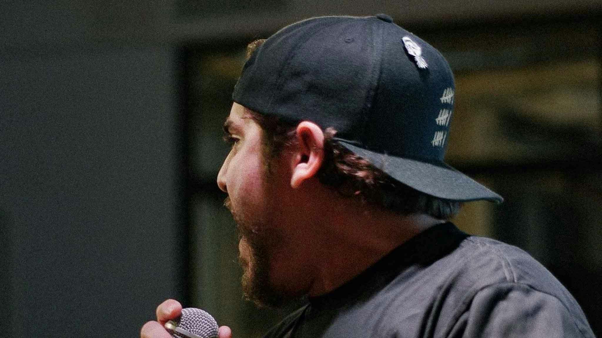 Louie C Rhymes performing live on stage wearing a backwards hat at an NFT conference.