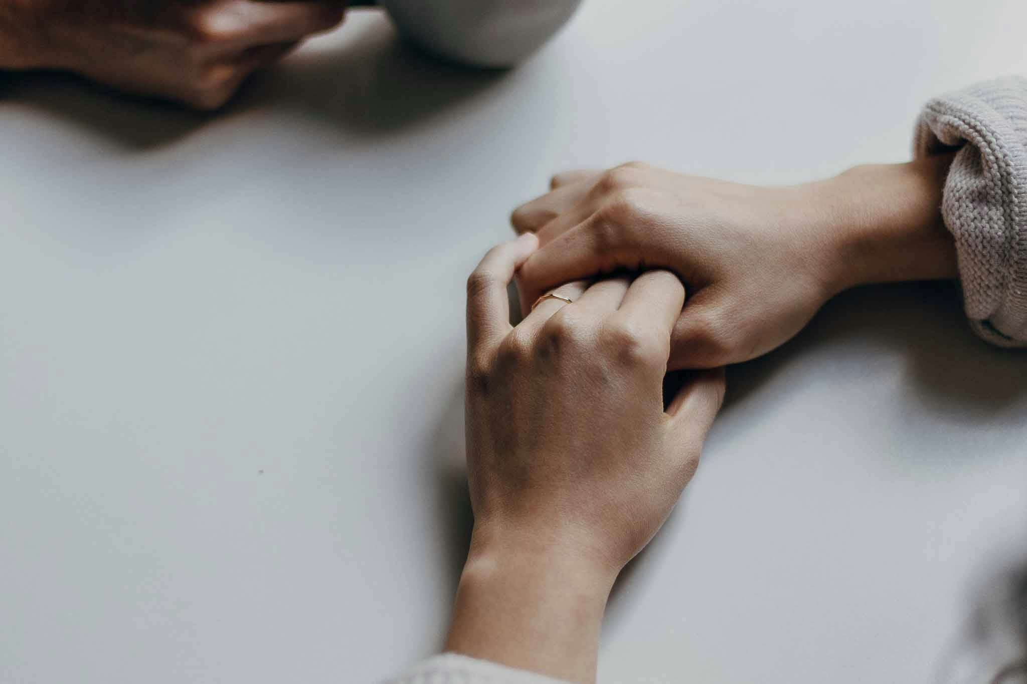 A woman's hands holding one another on a white table, next to a man holding a coffee cup