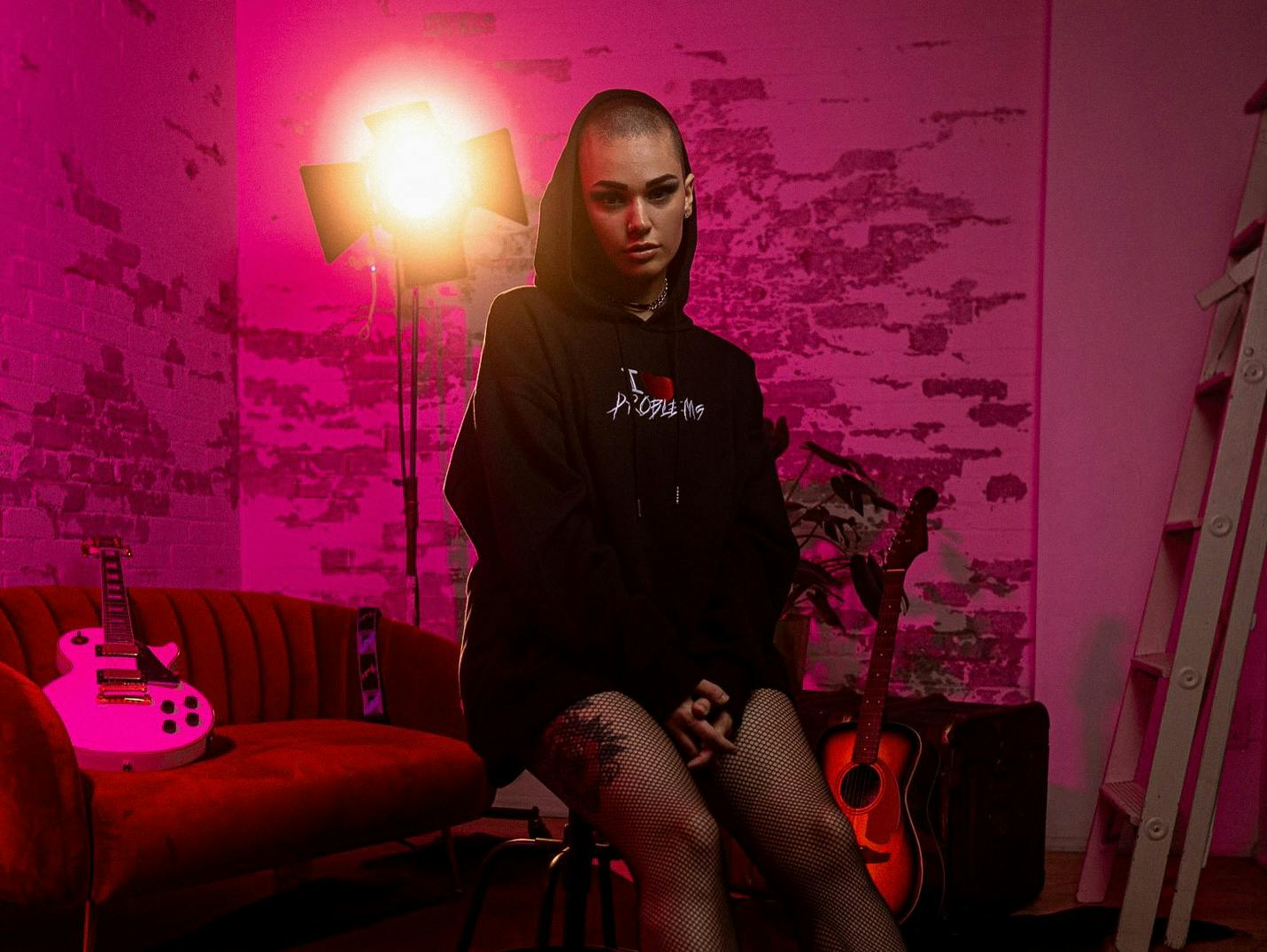 Female singer/songwriter Mela Bee sitting in a hoodie in a photography studio with purple lights.
