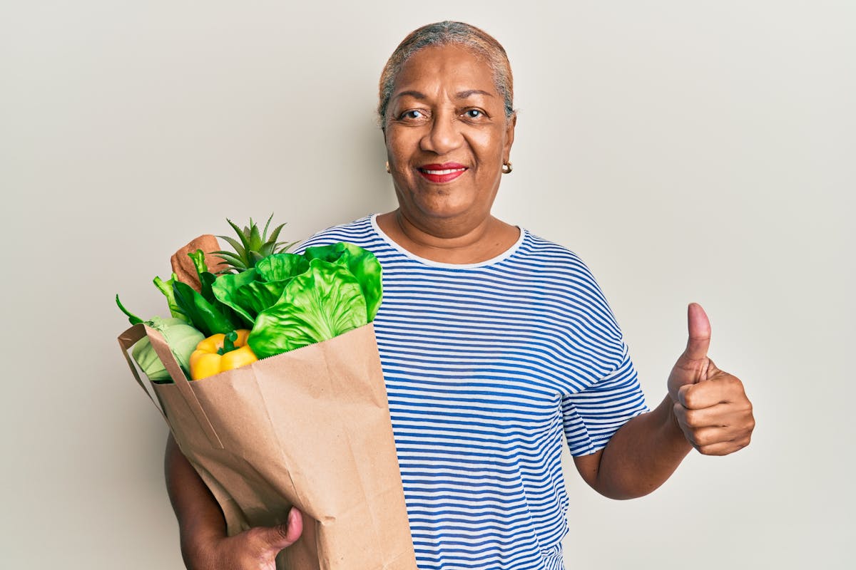 Woman holding a paper bag full of groceries making a thumbs-up 
