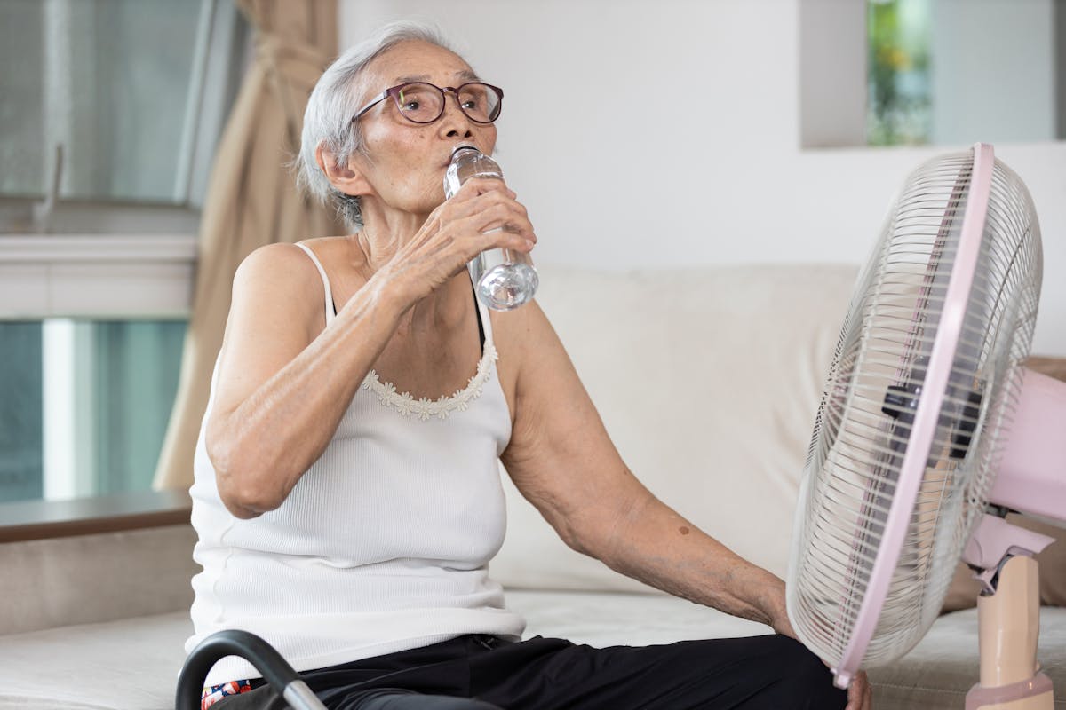 Old elderly woman drinking a bottle of water,keeping body water balance,drink a lot of water to prevent dehydration in heat hot summer weather while stay at home,prevention of heat stroke,health care