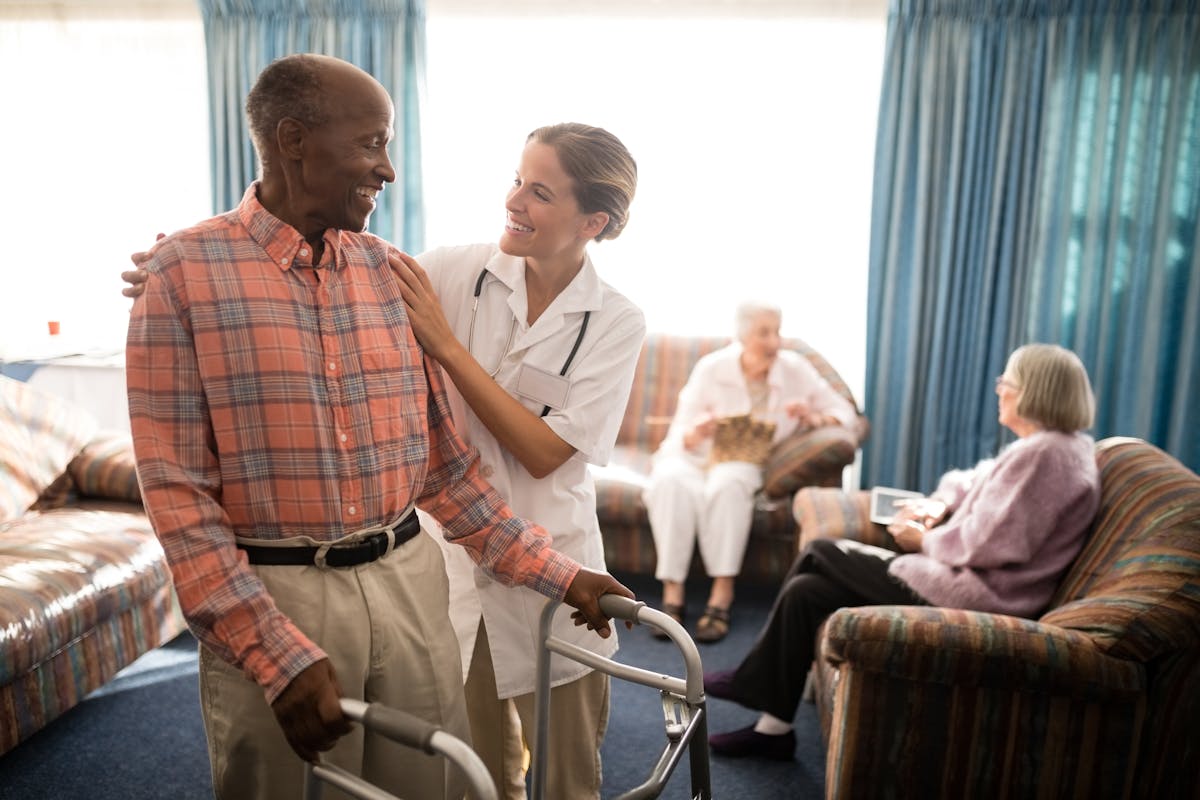 Smiling senior man with walker looking at female doctor against