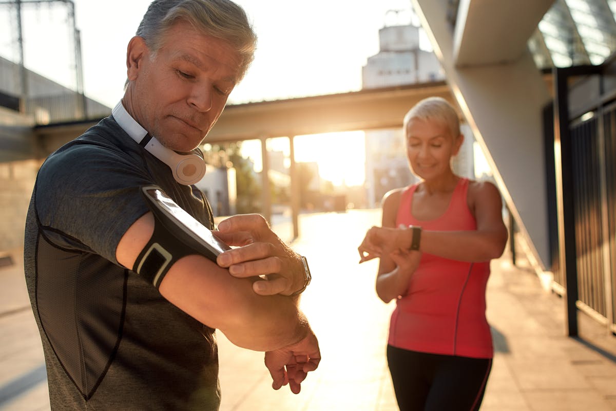 Using modern techologies. Active middle-aged couple in sports clothing checking training results while standing together outdoors. Checking pedometer