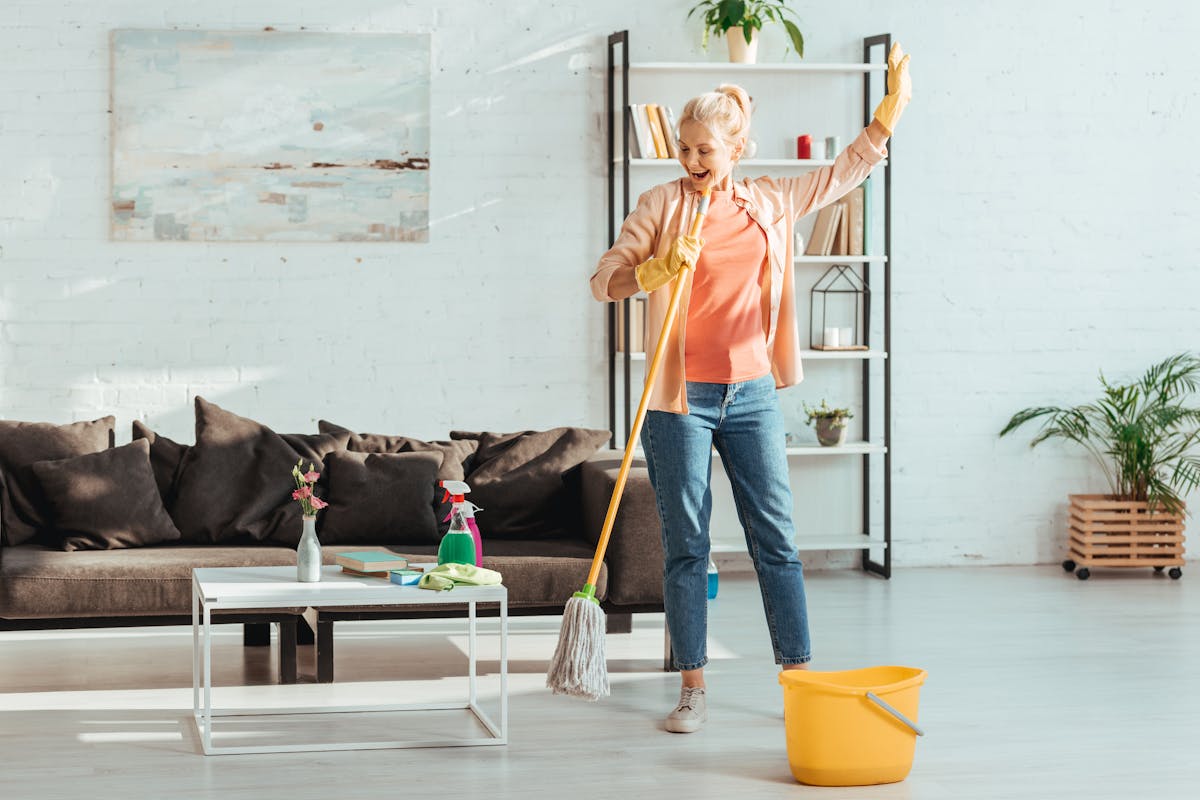 Full view of excited senior woman cleaning floor in living room