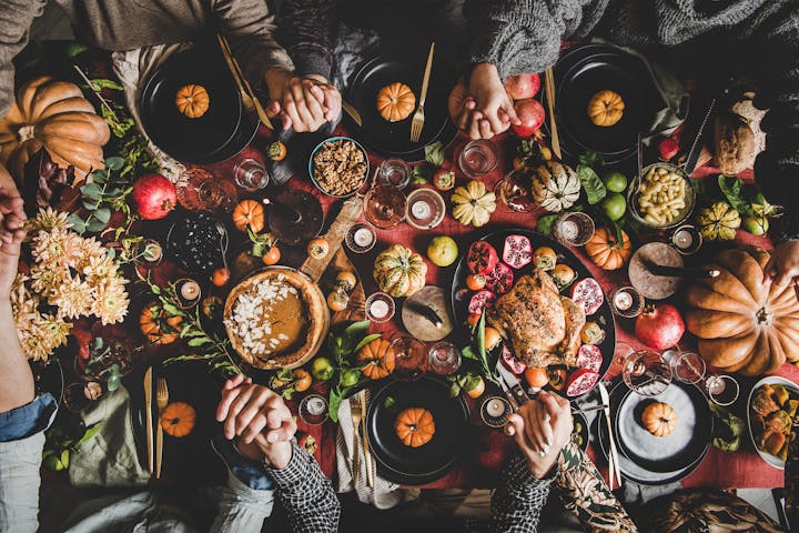 Family or friends praying holding hands at Thanksgiving celebration table

