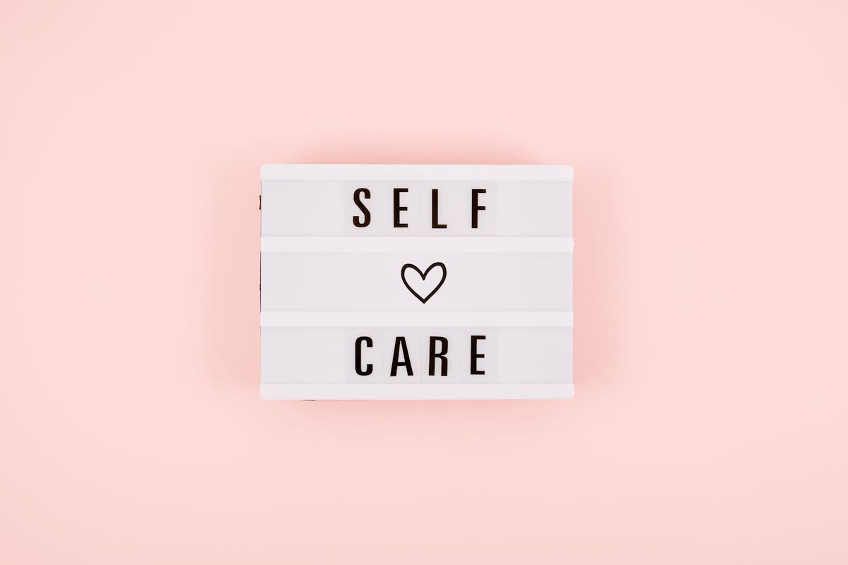 Self-care word on lightbox and flower narcissus on pink background flat lay. Take care of yourself.