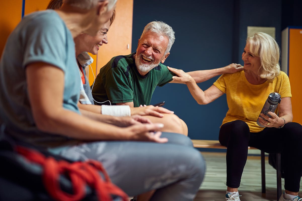 Group of four people in gym locker room, senior man and women talking after workout.