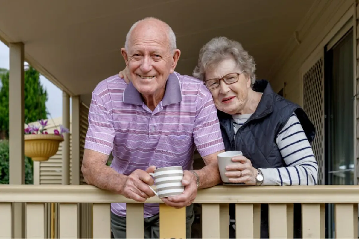 An older couple enjoys a relaxing moment together on their porch while holding cups of coffee.