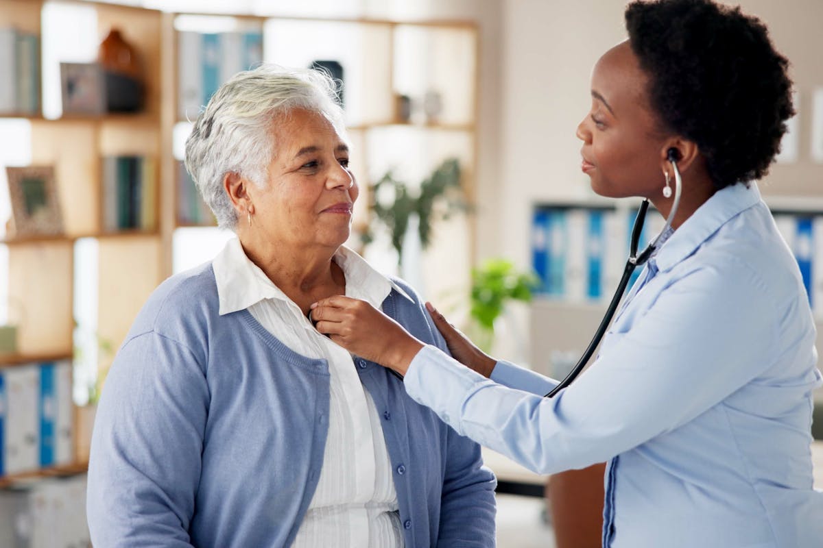 Woman, doctor and senior person with stethoscope, checkup or medical advice at clinic consultation. Help, healthcare and elderly patient in office with lung test, heart beat or chest exam in hospital