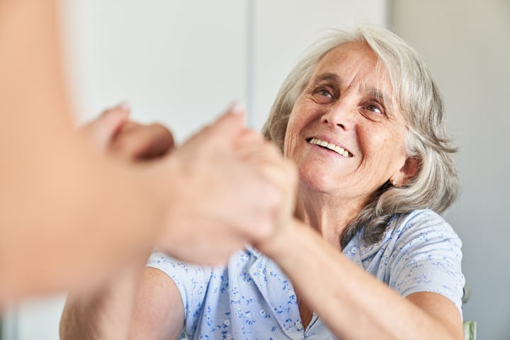 Elderly woman gratefully holds the hands of a geriatric nurse