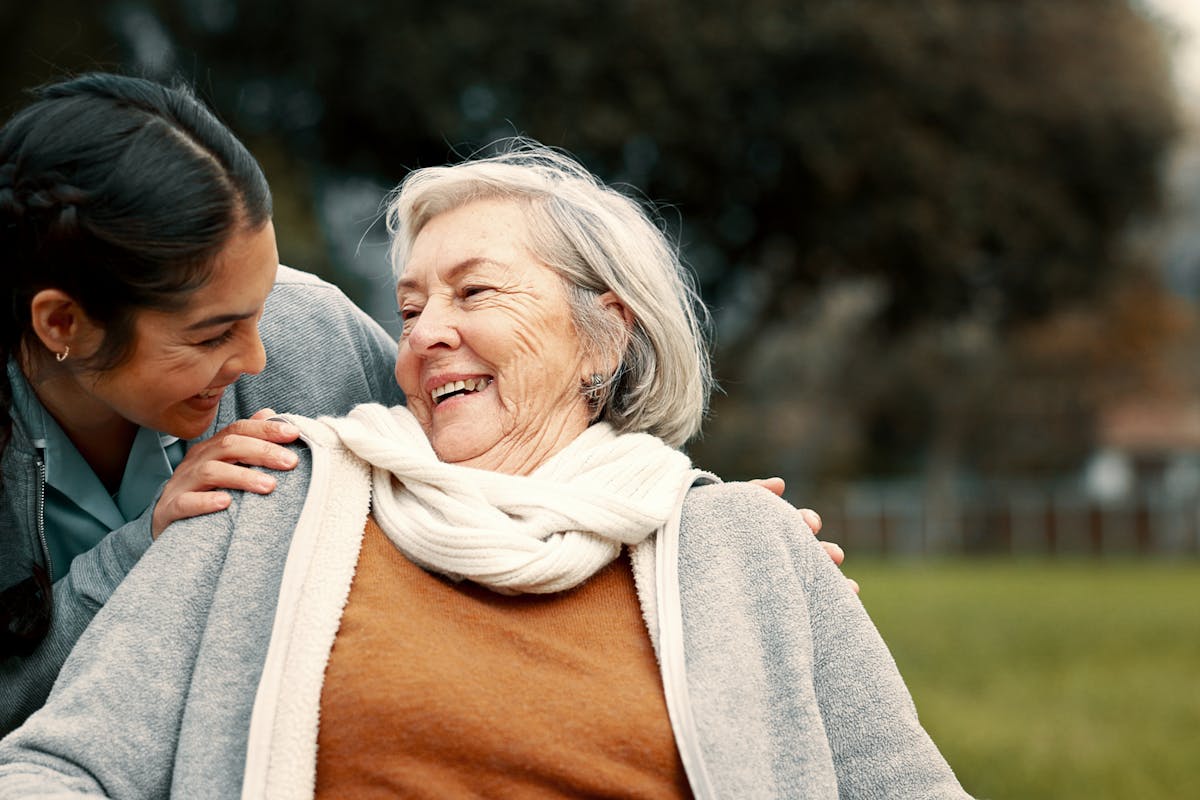 Caregiver helping woman with disability in park for support, trust and care in retirement. Nurse talking to happy senior patient in wheelchair for rehabilitation, therapy and conversation in garden