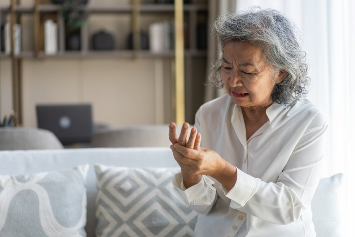 Elderly asian woman holding wrist pain, arthritis, health issue, senior female suffering from joint pain at home, expressing discomfort, aging health problem, chronic condition indoor living room