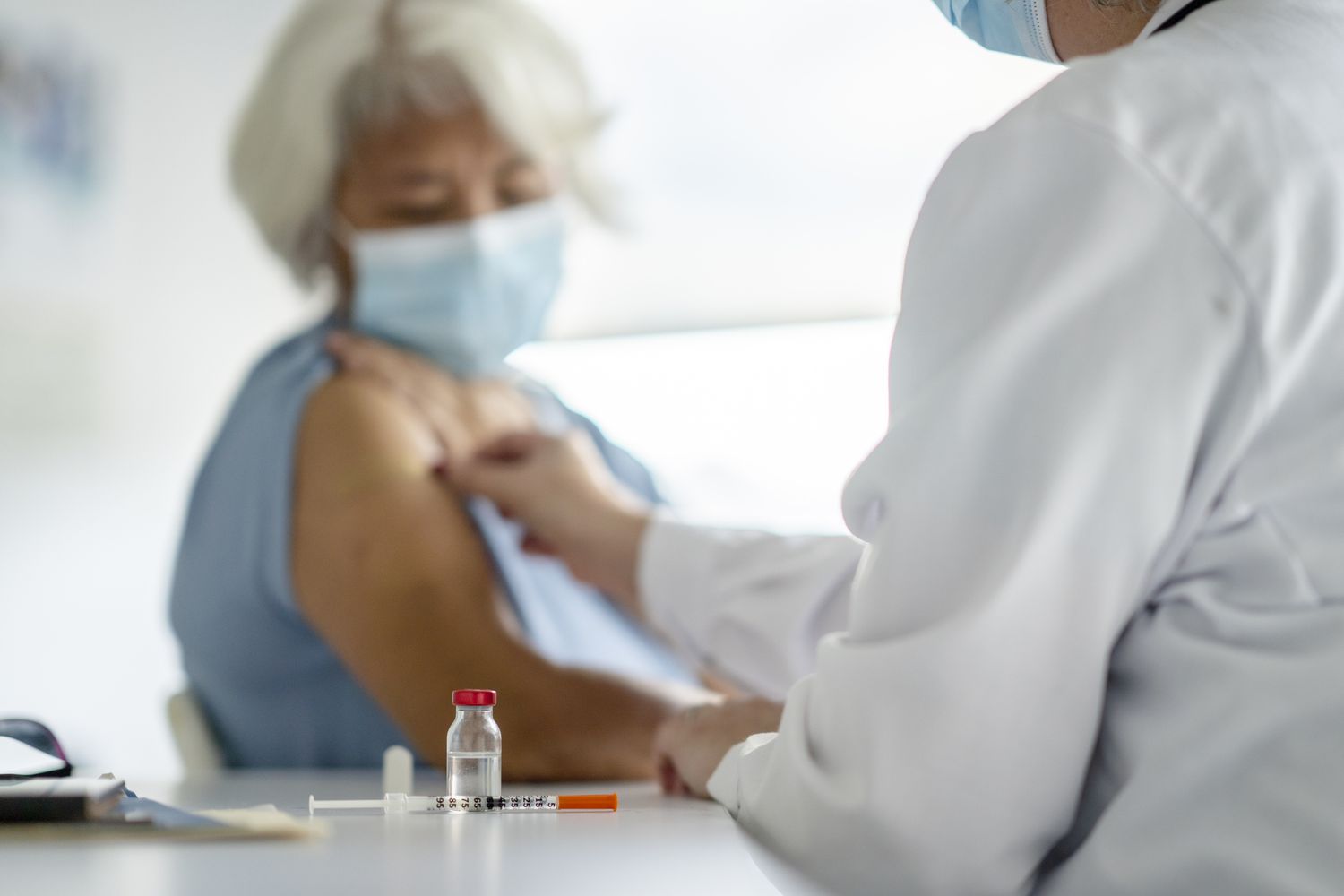 healthcare professional administering a vaccine injection to an older adult wearing a face mask in a clinical setting