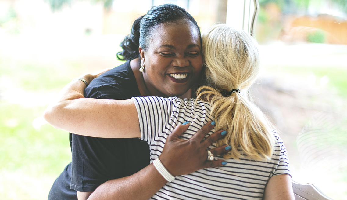 Two women warmly embrace, smiling with genuine happiness and comfort.