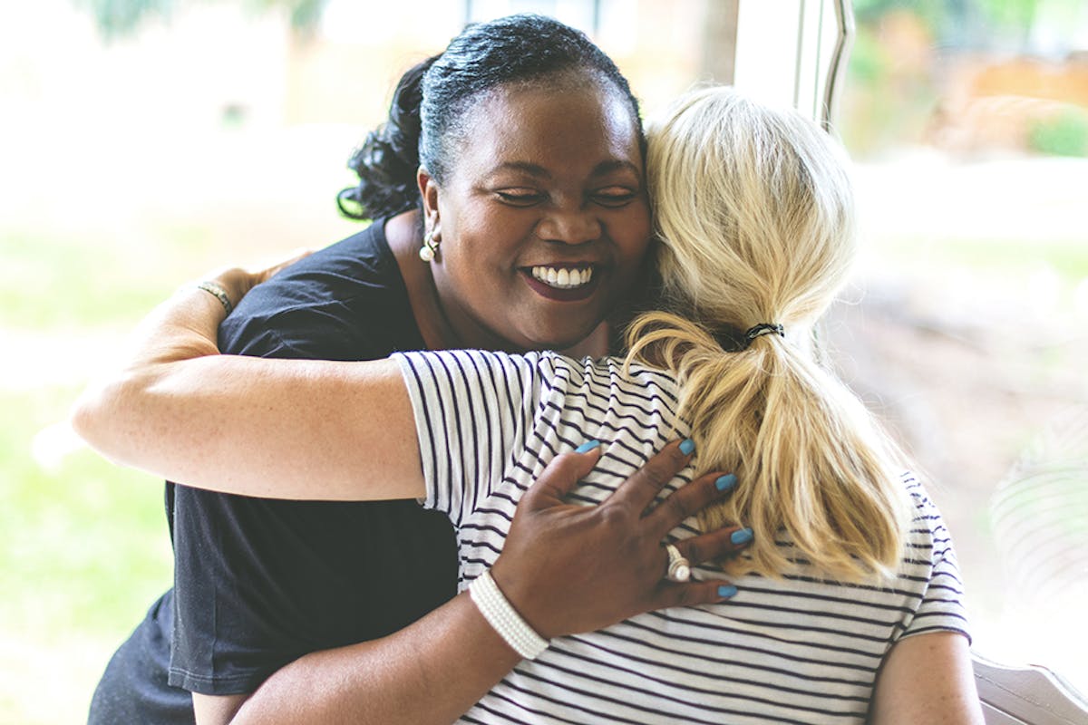 Two women warmly embrace, smiling with genuine happiness and comfort.
