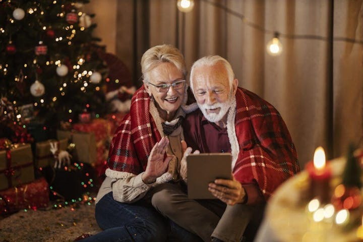 older couple sitting closely together in a warmly lit living room decorated for the holidays