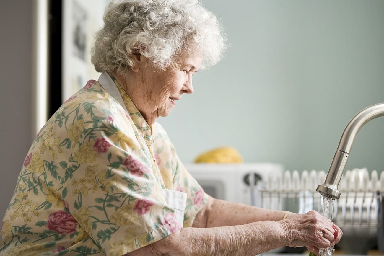 An older woman carefully washing produce at her kitchen sink, highlighting everyday independence and home safety.