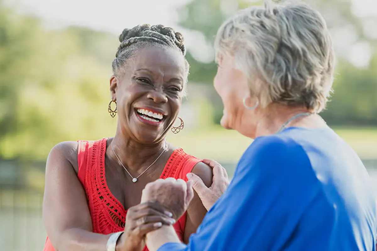 Two older women share a joyful moment outdoors, highlighting the warmth and connection that come from meaningful social relationships.