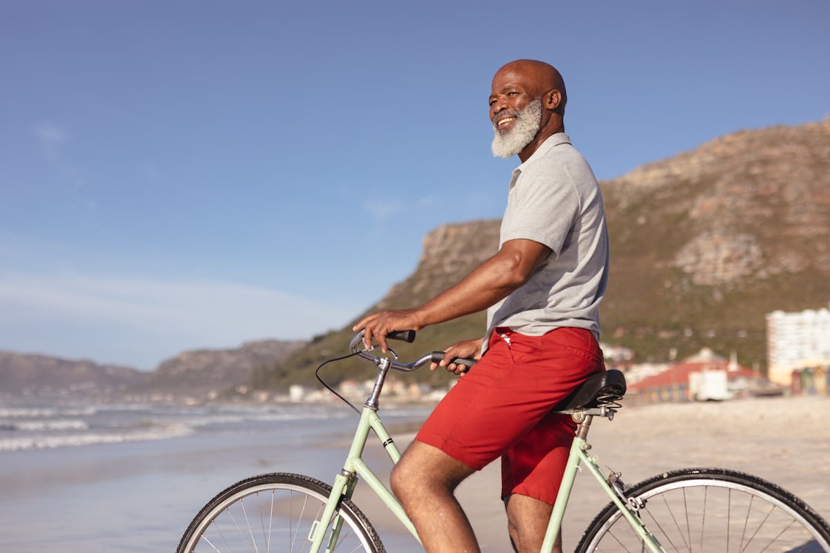 Senior african american man sitting on bicycle smiling on the beach
