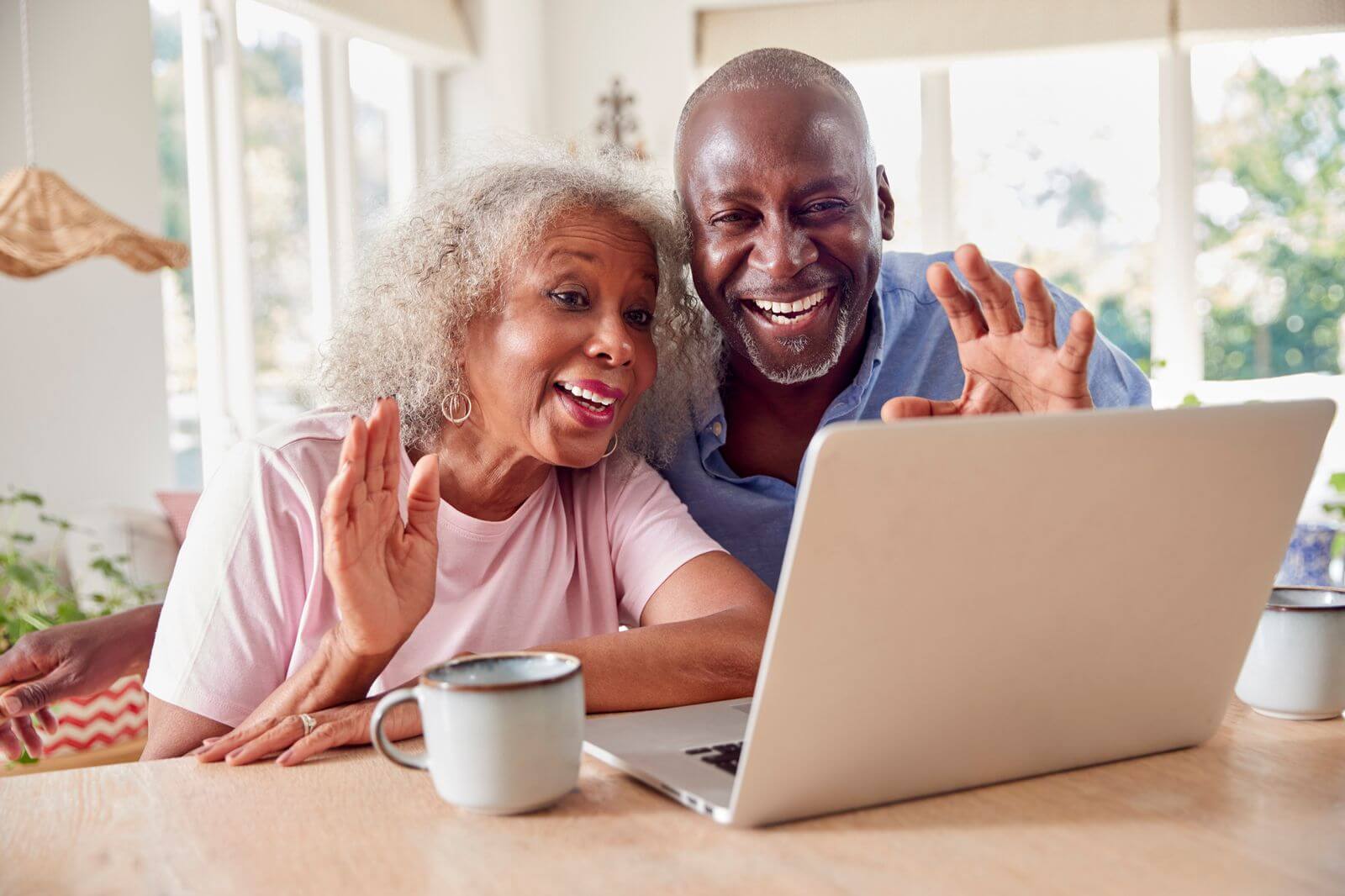 An older couple smiles and waves during a video call on a laptop, showcasing how technology helps seniors stay connected with loved ones.