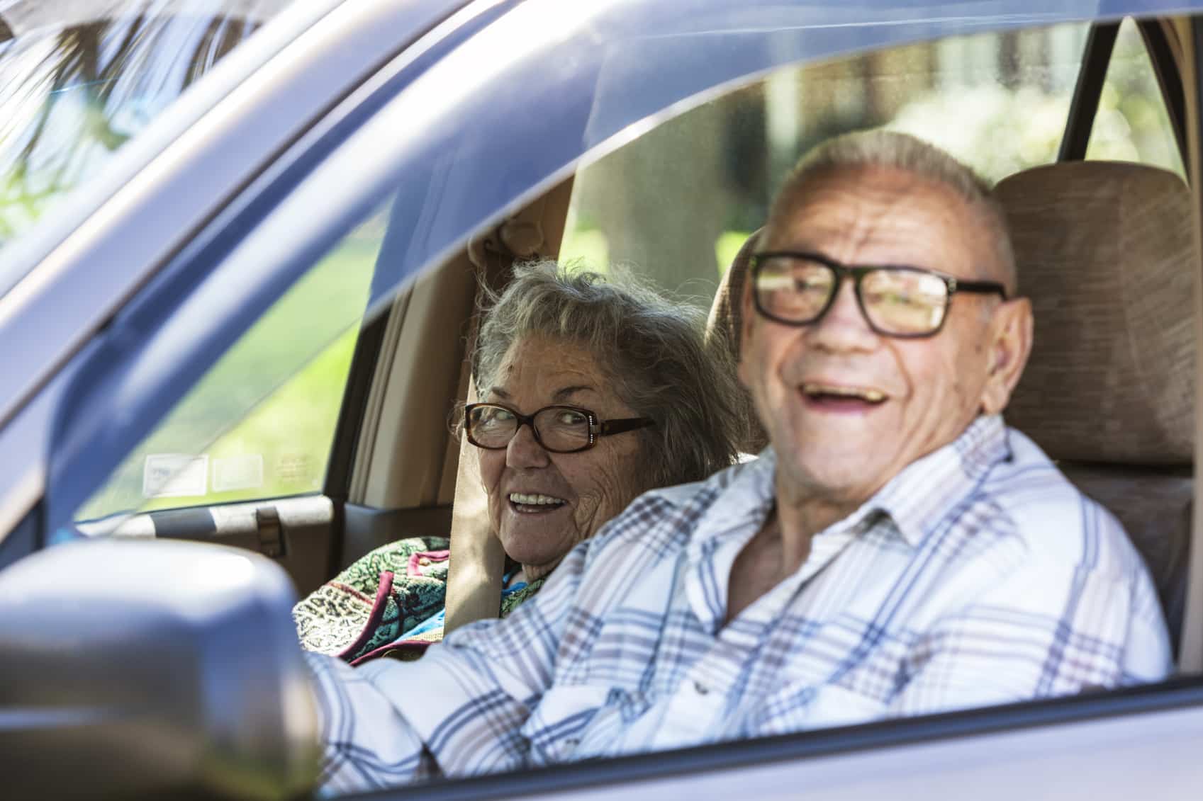 A smiling senior couple sits together in a car, enjoying a drive while embracing the freedom and independence of staying active on the road.