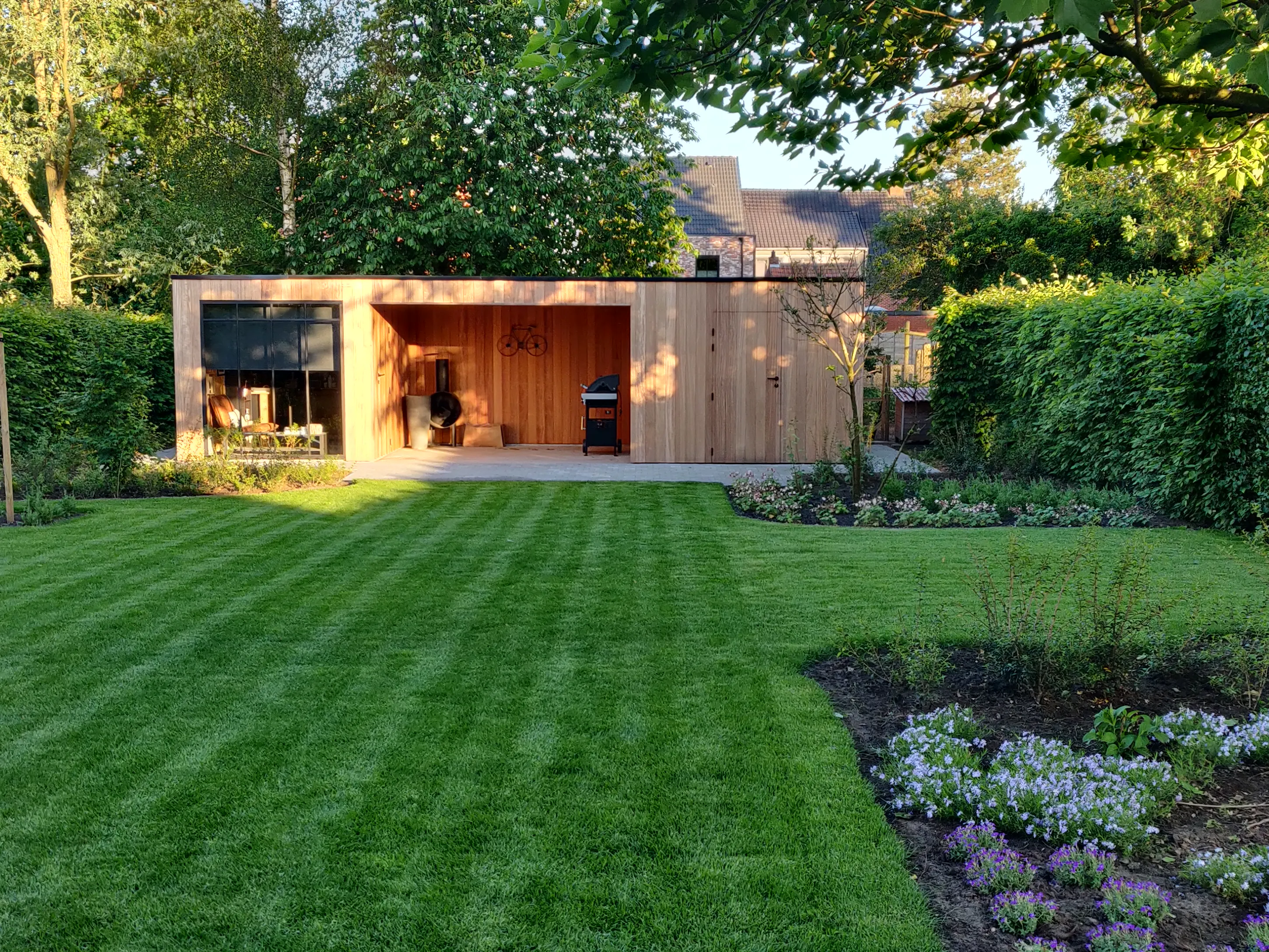 Moderne houten tuinberging met overdekte relaxruimte, plat dak, omgeven door een ruime groene tuin.