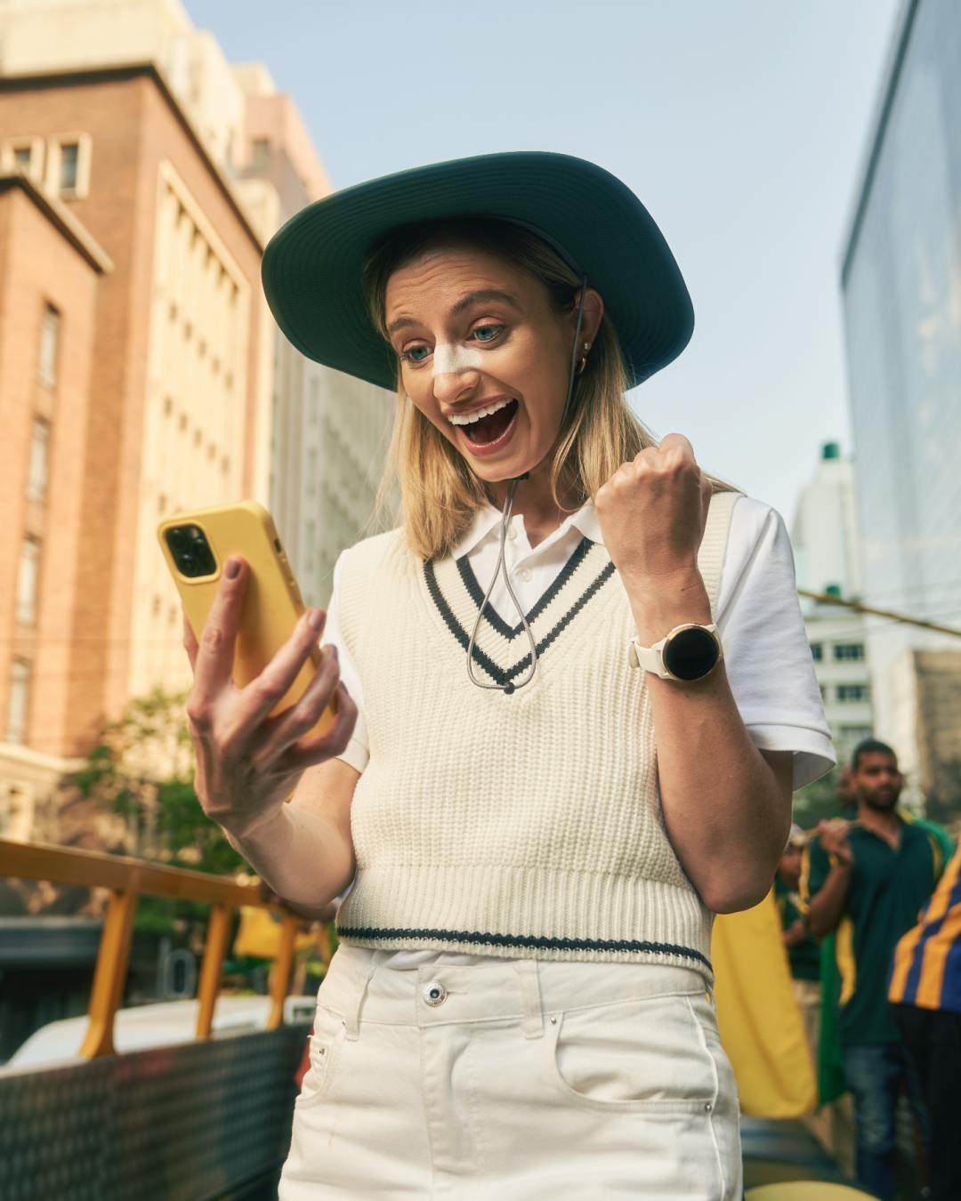 A woman stands celebrating as she looks at her phone