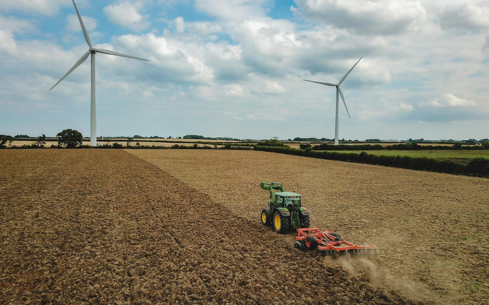 Two wind turbines behind muddy land with tractor working on it