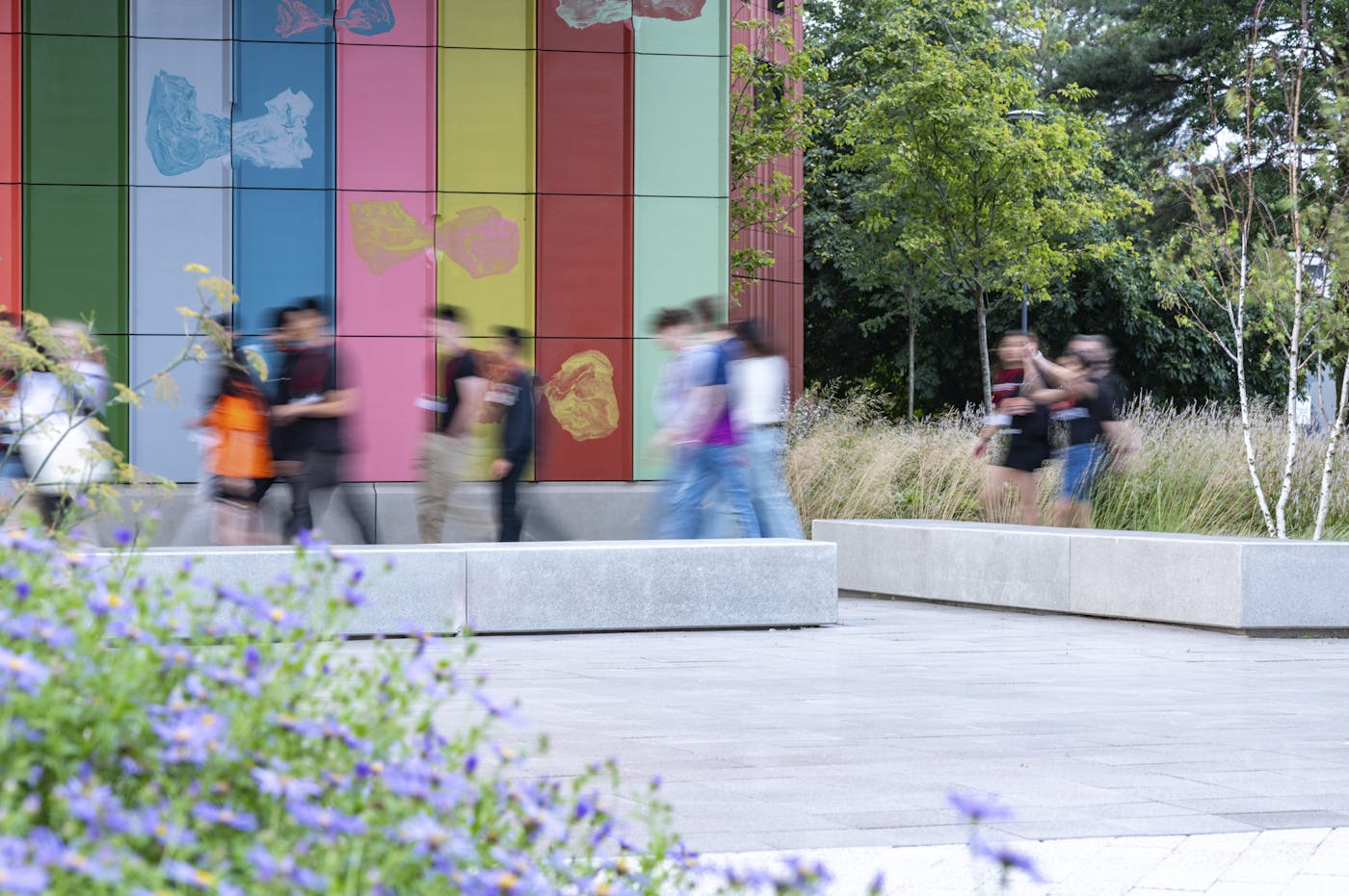 Crowd of people walking past stone benches with motion blur