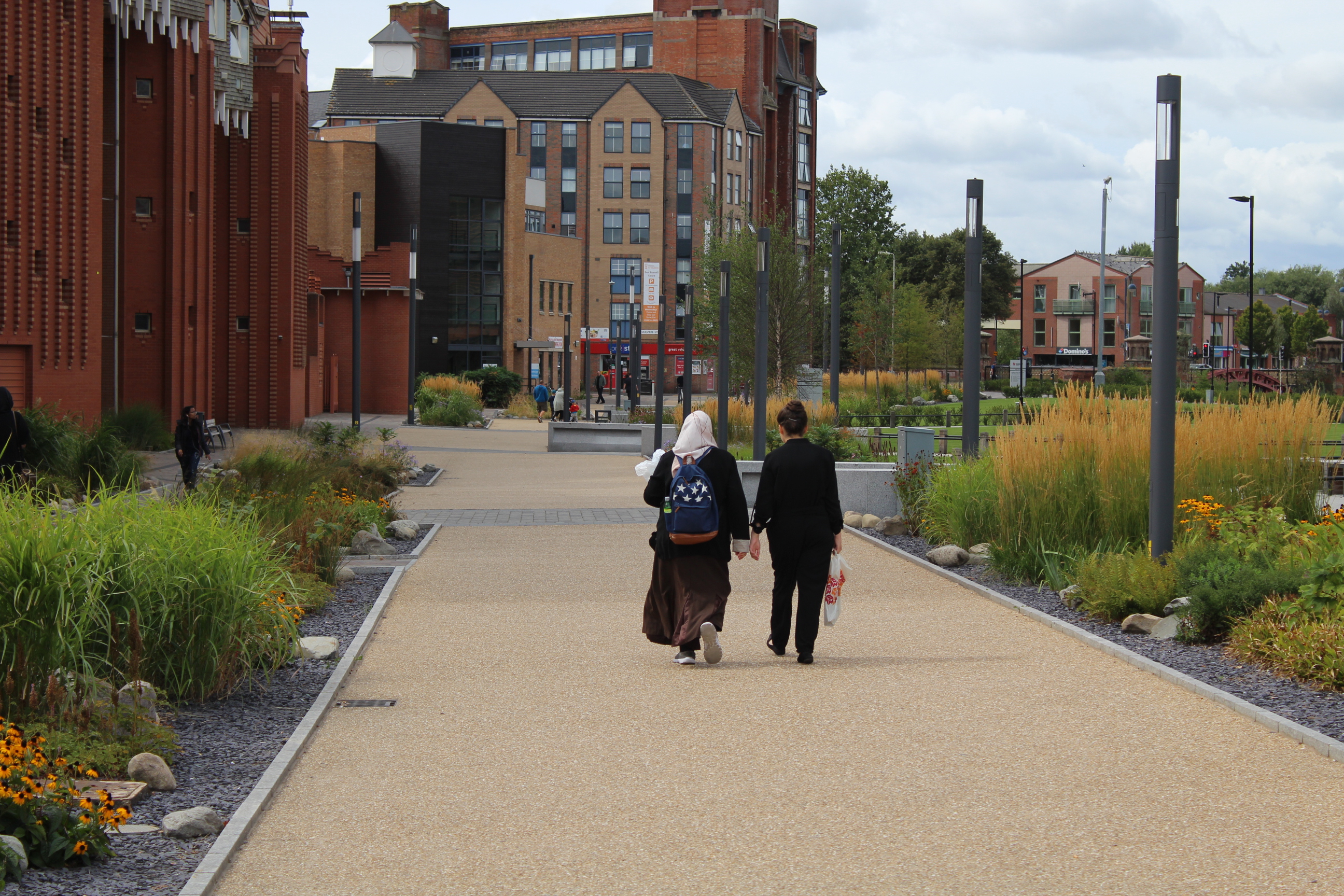 two people walking through a modern street with plants