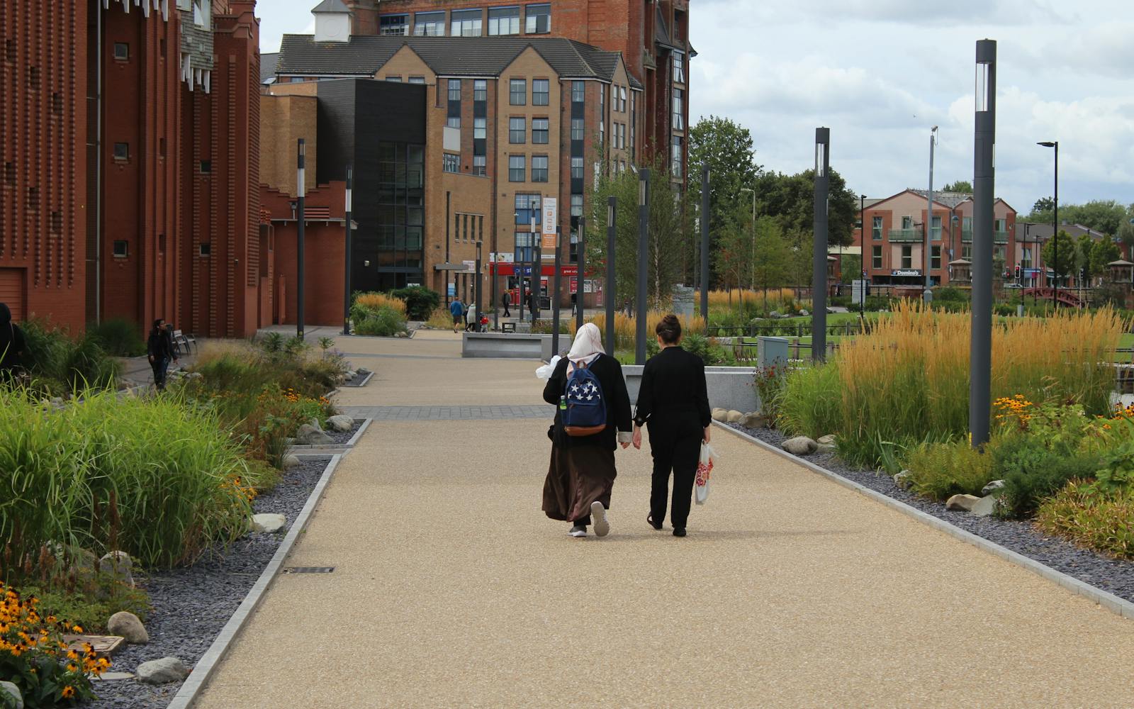 two people walking through a modern street with plants