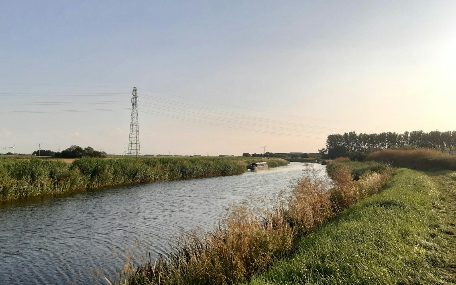 River in grassy rural area with overhead power lines and pylon