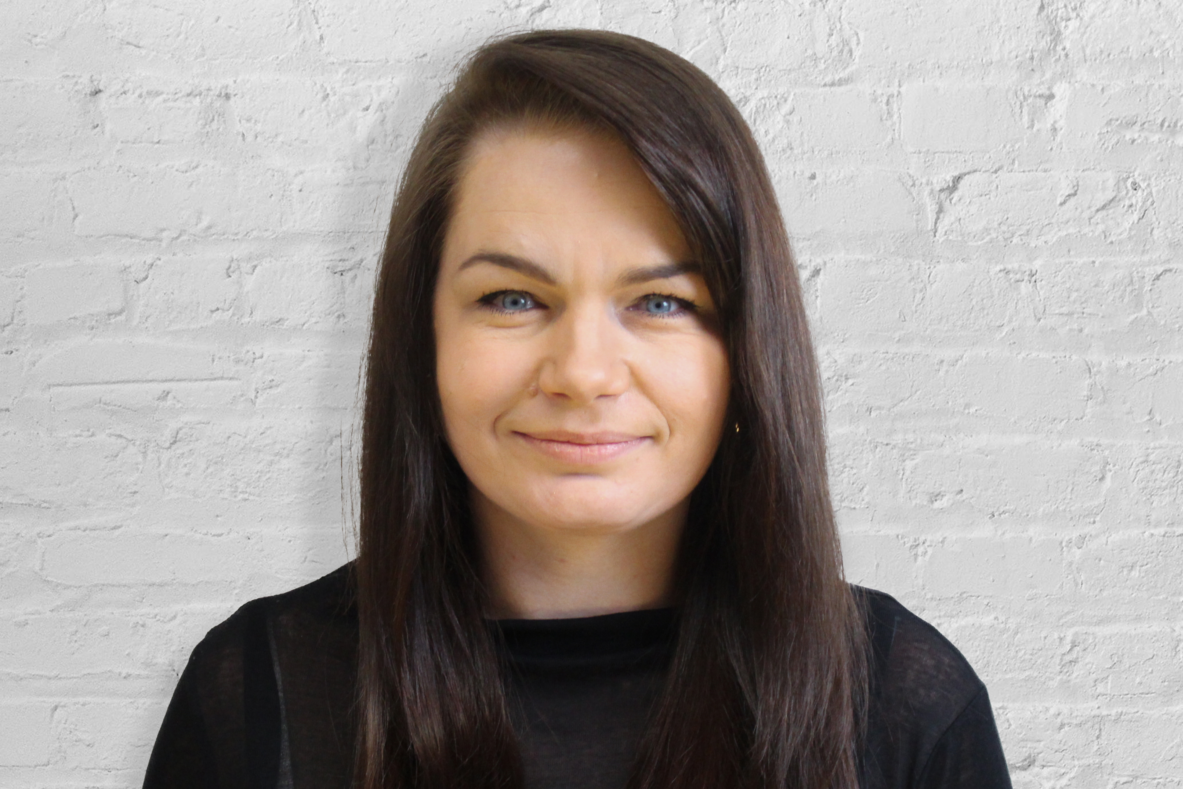 Person smiling in front of white brick wall