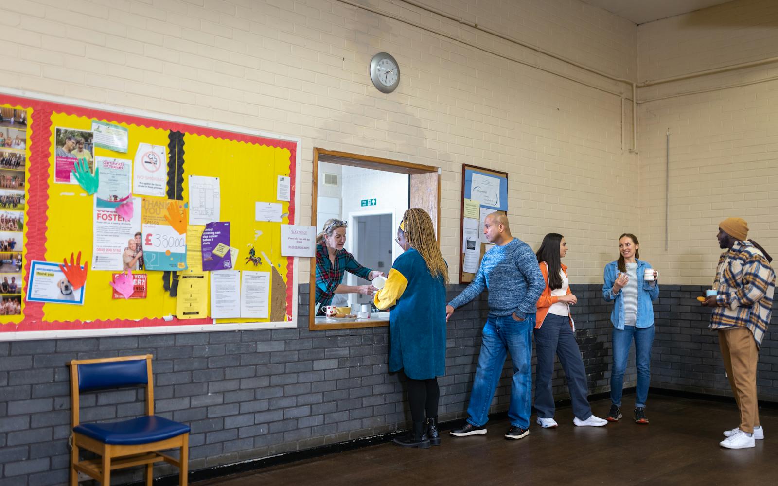 A queue of people standing together, waiting to be served hot drinks through a hatch.