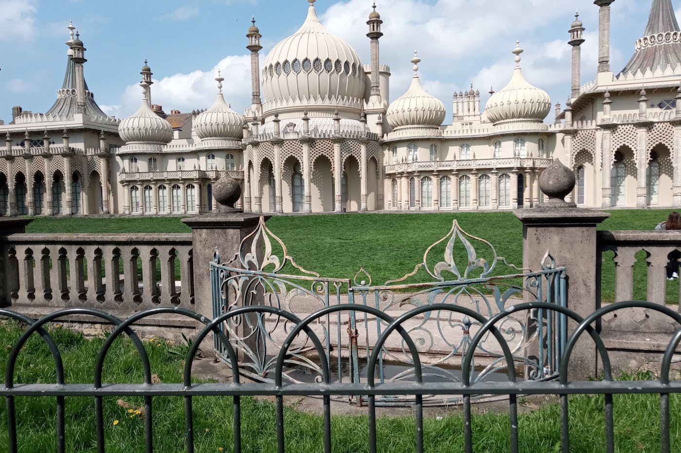a large white building with a fence and grass with Royal Pavilion in the background