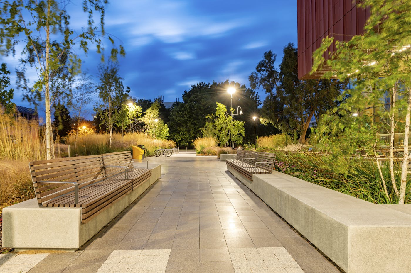 Building in paved area with outdoor furniture and street lighting in dusk