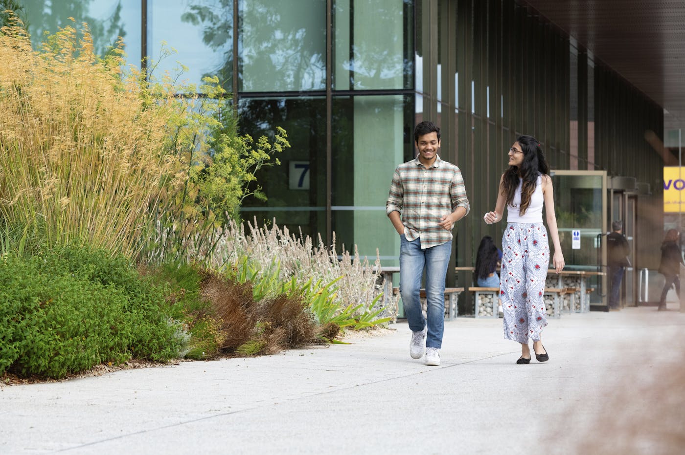 Two people walking on path alongside shrubbery