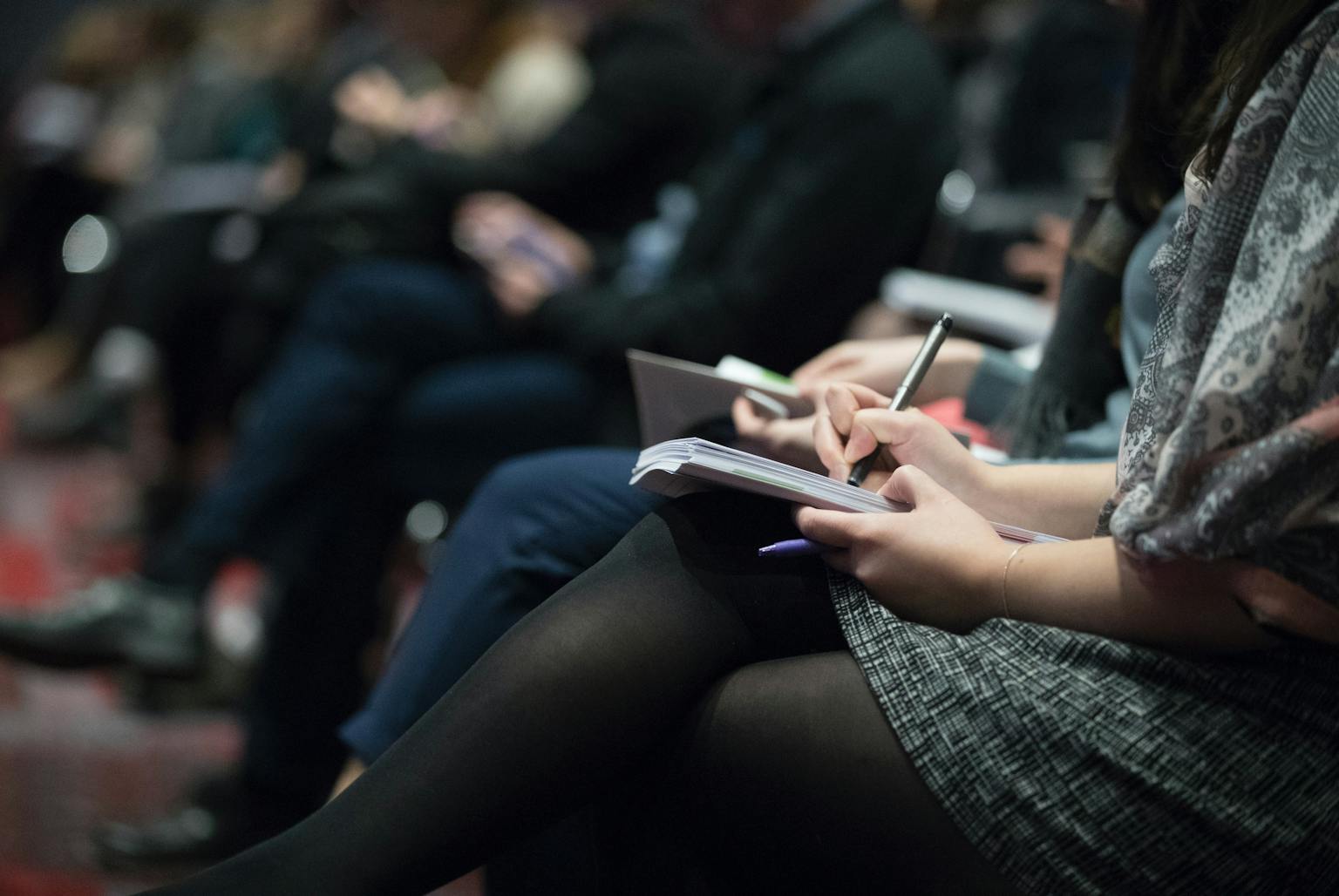 Person sitting at conference writing notes on paper pad