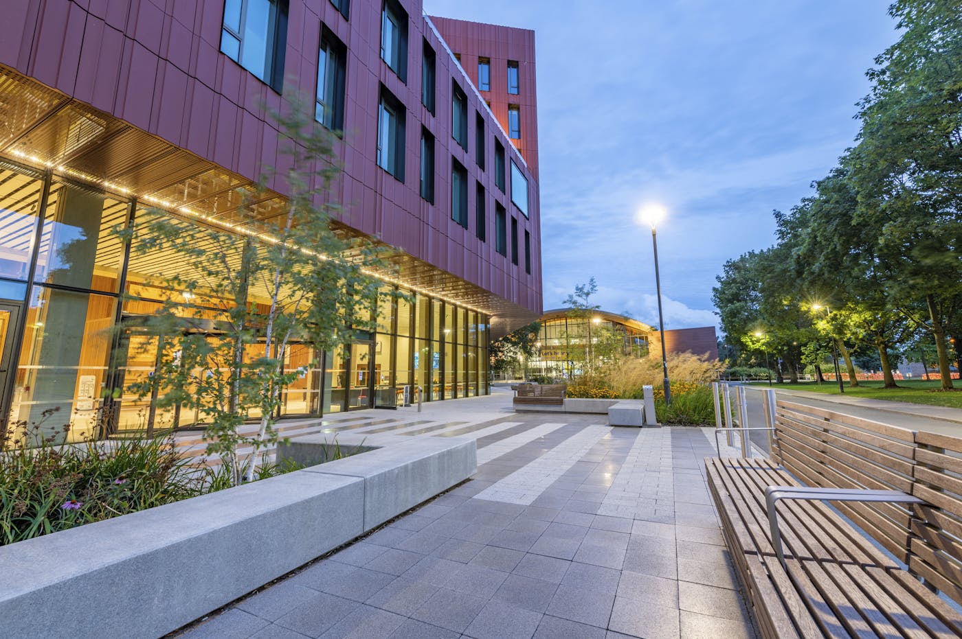 Building in paved area with outdoor furniture and street lighting in dusk