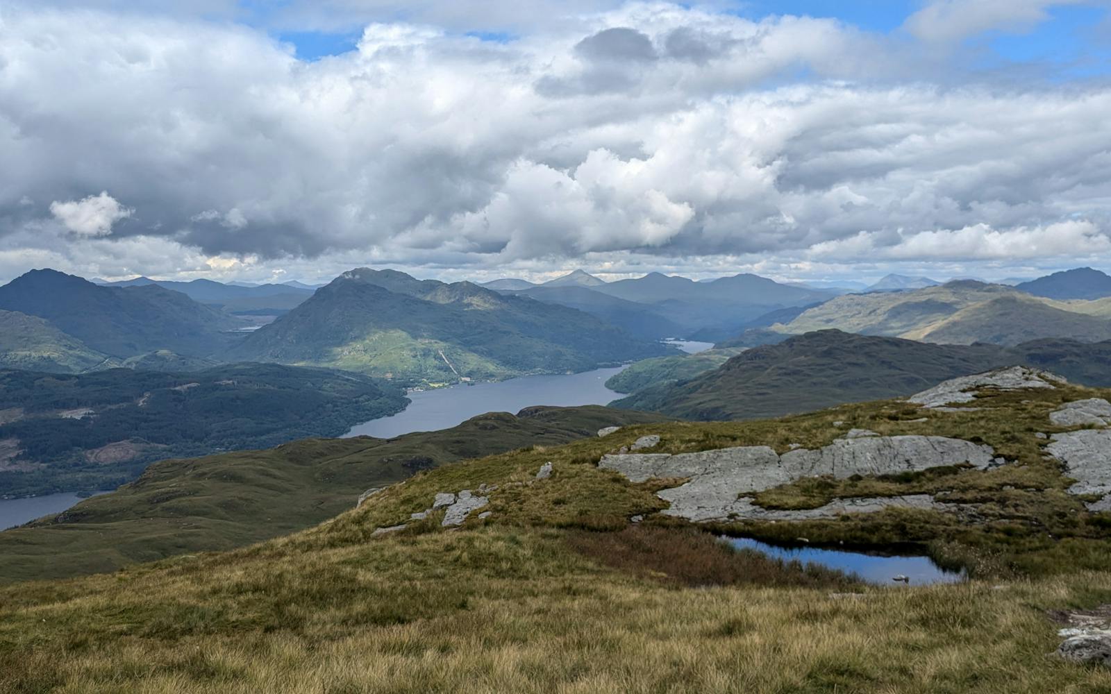 A view over a Scottish landscape with mountains in the background and a loch