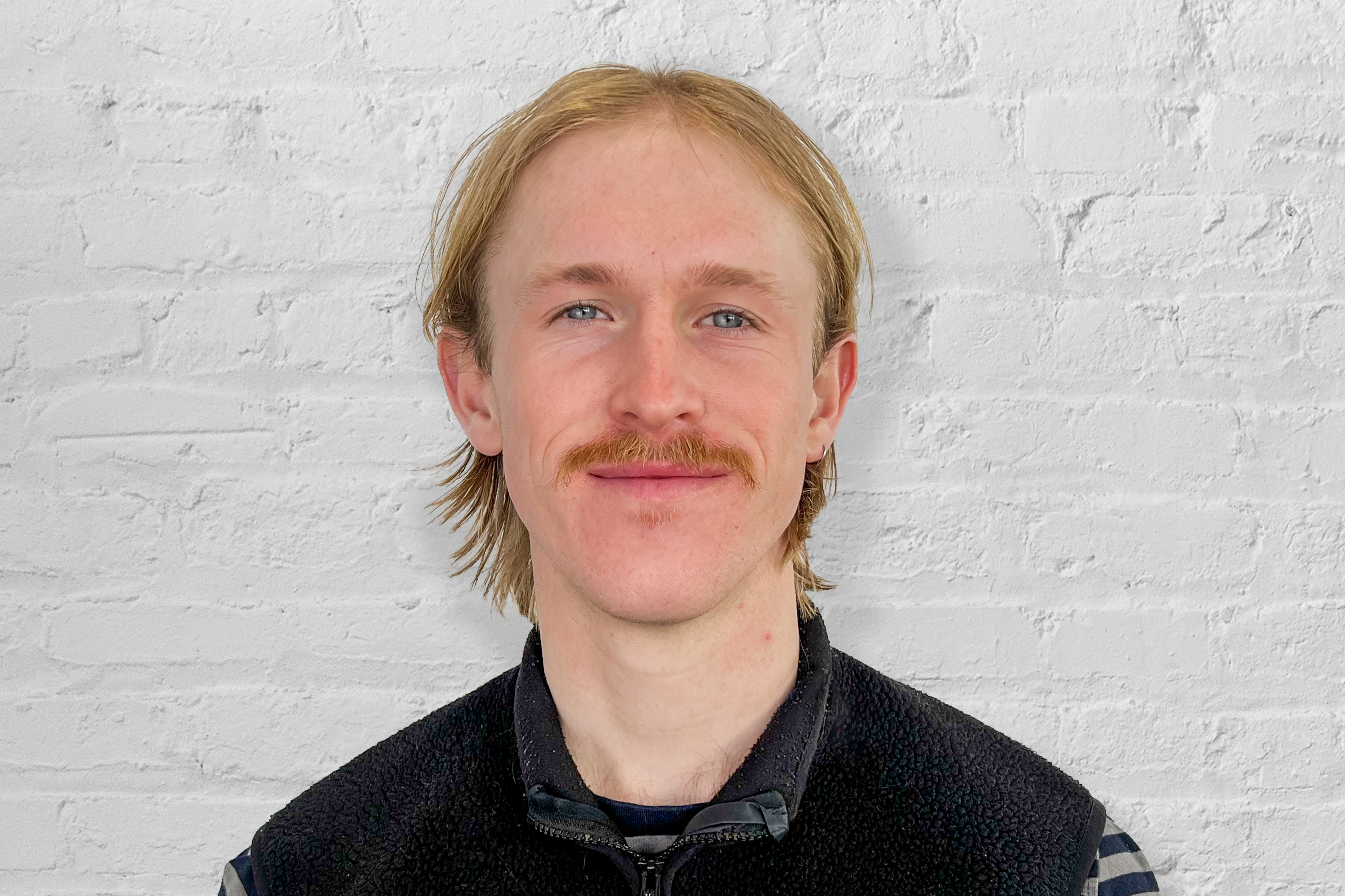 A professional headshot of Patch Tully in front of a white brick wall.