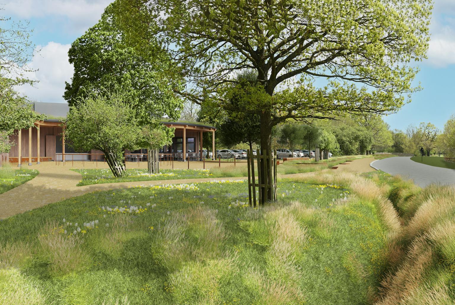 Two similar renderings show a modern, light-brown building with a covered walkway next to a road in a park-like setting. Trees and parked cars surround the building. The top image shows a view from across the road, while the bottom image is a closer view from a slightly different angle on the same side of the road as the building.