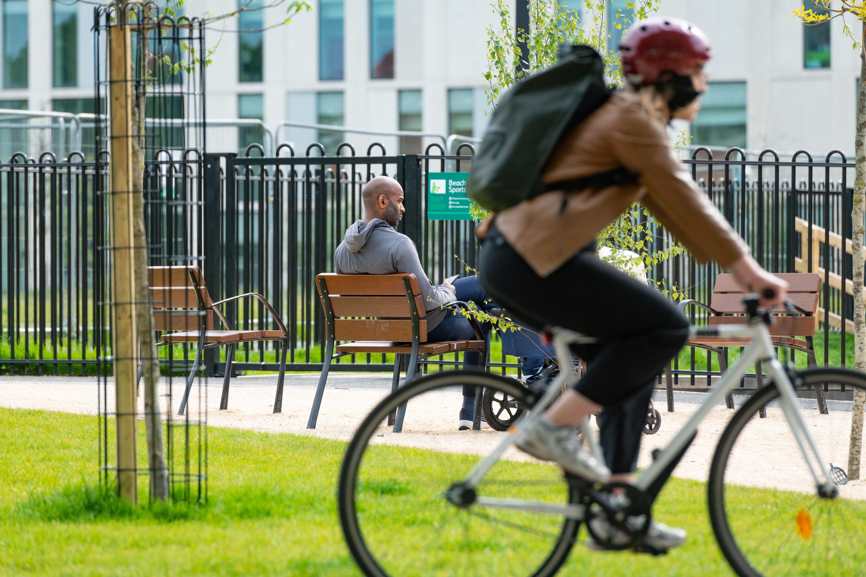 a woman riding a bike in a park with a man sitting on a bench